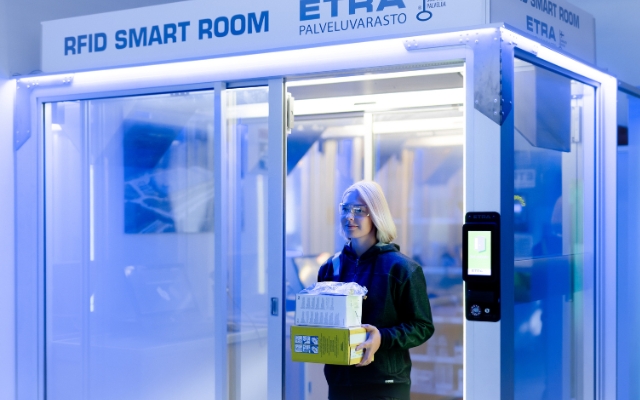 A woman exiting an Etra RFID Smart Room carrying several boxes of industrial supplies, demonstrating automated inventory tracking in a high-tech service storage environment.