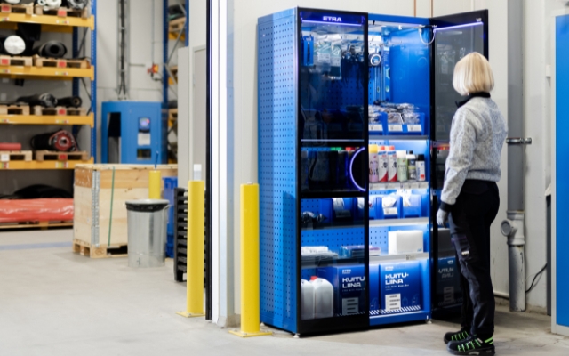 En kvinna använder ett Etra-automatskåp med underhålls- och rengöringsprodukter i en industrimiljö.