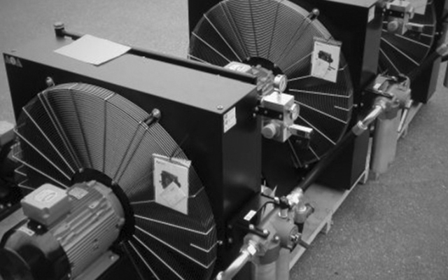 Row of industrial oil coolers with large fan units, electric motors, and hydraulic components, installed on a pallet in an outdoor or factory setting.