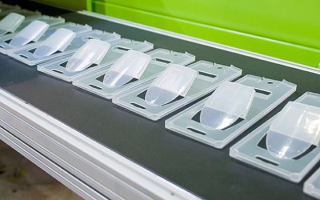 Plastkomponenter tillverkade av Okartek på en grå yta. Varje komponent har ett transparent, kupolformat lock och en rektangulär bas.